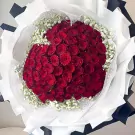 Bouquet of 99 vibrant red roses and white gypsophila flowers, artfully arranged and wrapped.