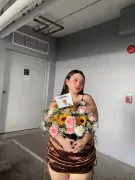 A woman holds a "Little Happiness Box" flower arrangement with sunflowers and pink roses.