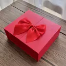 Red gift box with a red satin bow on a wooden surface.
