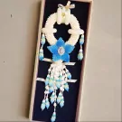 White jasmine malai with blue centerpiece and dangling blue flower accents in a gift box.