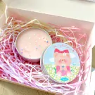 Two pink candles with star glitter in a gift box with pink shredded paper.