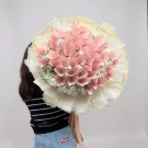 A person holds a large bouquet made of pink folded banknotes and white baby's breath flowers.