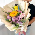 Bouquet with a yellow plush chick wearing a graduation cap, a sunflower, pink roses, and purple and green filler flowers.
