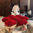 A couple hugs in front of a large display of 1000 red roses.