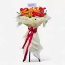 A floral stand with red and orange gerbera daisies, wrapped in pale yellow paper and tied with a red ribbon.