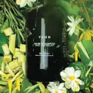 Dark green bottle of YAHN Hair Shampoo surrounded by fresh herbs and white flowers.