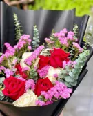 A bouquet of red and white roses with pink statice flowers, wrapped in black paper.