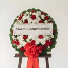 Funeral wreath with red and white flowers on a stand, bearing a condolence message.