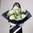 A bouquet of white roses, baby's breath, and eucalyptus wrapped in navy paper with white ribbon.