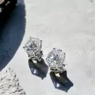 Two oval-cut moissanite diamond earrings with silver settings on a light gray textured surface.