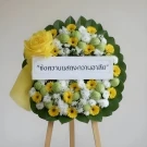 Funeral flower wreath with white chrysanthemums, yellow gerberas, green leaves, and a yellow ribbon.