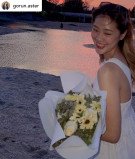 Woman in white dress holding white roses and gerberas bouquet at sunset.