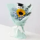 Graduation bouquet with a sunflower, baby's breath, and a graduation cap-wearing plush toy, wrapped in mint paper and tied with a white ribbon.