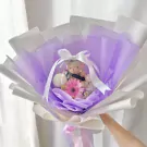 Graduation bouquet with teddy bear in clear balloon, surrounded by purple and white wrapping.
