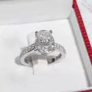 Oval-cut moissanite diamond ring with pavé band in a jewelry box.
