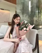 Woman in floral dress holding a pink rose and eucalyptus bouquet.