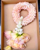 A floral garland with pink petals and pastel roses in a box.