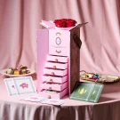 Pink chocolate box with stacked drawers, red roses, chocolates, and cards.