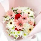 A bouquet of pink gerberas, white carnations, red carnations, and small pink roses wrapped in pale pink paper.