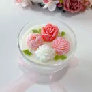 Candle in a glass bowl with carved floral wax art, including pink roses and white flowers.
