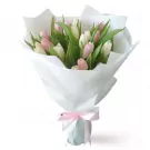 A bouquet of white and pink tulips wrapped in white paper, tied with a pink ribbon.