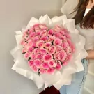 A large bouquet of 50 vibrant pink roses wrapped in white paper, held by a person.