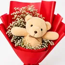 Teddy bear peeking from a bouquet of white flowers in red wrapping.