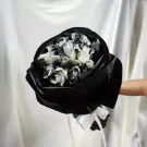 Bouquet of black and white roses wrapped in black paper, held by a person with a tattoo on their arm.