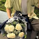 A bouquet of white roses with gypsophila and eucalyptus, wrapped in navy blue paper.