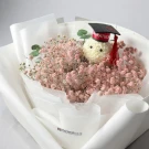 A graduation bouquet with a teddy bear wearing a cap, surrounded by pink baby's breath flowers.