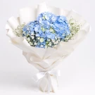 Blue hydrangeas and white baby's breath in white paper wrap, tied with a white ribbon.