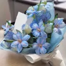 Bouquet of light blue and white flowers with delicate petals, wrapped in pale blue and white paper.