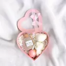 Pink heart-shaped spa gift box containing rose bath salts, a bath bomb, and fluffy white towel artfully arranged as a teddy bear.
