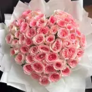 Heart-shaped bouquet of 50 delicate pink roses, wrapped in white tissue paper.