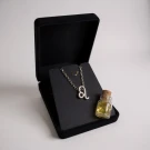 A silver Leo zodiac necklace in a black velvet box with a small glass vial of yellow liquid.