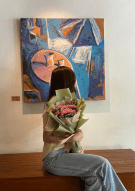 Person holding pink carnation and dusty miller bouquet in front of abstract painting.