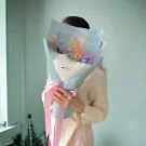 Person holding a bouquet of colorful velvet wire flowers wrapped in pale blue and white paper with pink ribbon.