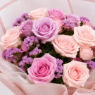 Pastel pink and purple rose bouquet wrapped in delicate pink paper with a ribbon.