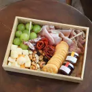 Charcuterie board with grapes, cheese, cured meats, nuts, crackers, and jam jars.
