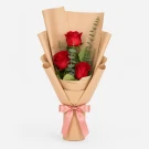 Three red roses wrapped in brown paper with a pink ribbon.