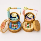 A 2-tier traditional bamboo basket set featuring a delicate garland and artisanal Thai desserts on fresh floral beds