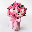 Pink and white carnation bouquet in a pink vase with a pink ribbon bow.