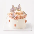 White cake with pink frosting, butterfly decorations, and "Happy Birthday" topper.