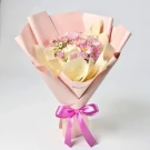 Bouquet of pink daisies, white roses, and chamomile in blush paper, tied with a pink bow.