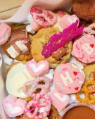 Sweet treats assortment including cookies, brownies, marshmallows, and pretzels decorated with pink icing and sprinkles.