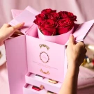 Pink gift box with red roses and chocolate drawers, held by hands.