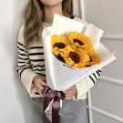 Woman in striped sweater holding bouquet of sunflowers wrapped in white paper, tied with a brown ribbon.