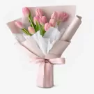 Bouquet of pink tulips with green leaves, wrapped in pink and white paper, tied with a pink ribbon.
