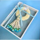 A floral garland of white jasmine with blue and green rose accents in a white box, tied with blue ribbon.
