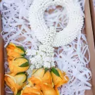 A white floral garland and yellow roses in a box with white crinkle paper.